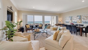 A spacious living room with a large window overlooking the ocean, furnished with sofas and chairs, and a dining area with a table and chairs. - Tuscany Sunrise - A Luxury Retreat for Discerning Guests (Navarre)