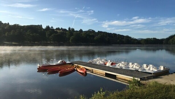 Een rustig meer met een steiger die het water in reikt, met verschillende kano's en een rij roeibootjes.