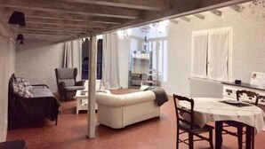 Een gezellige woonkamer met een bank, een eettafel met stoelen en een keuken in de achtergrond.
