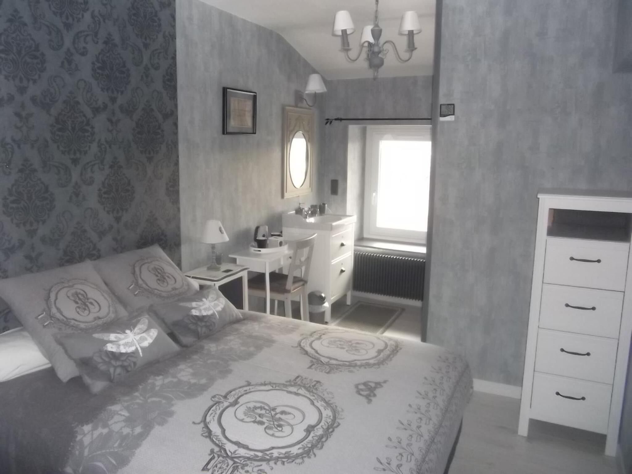 A bedroom with a bed, a desk, a dresser, and a window.
