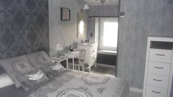 A bedroom with a bed, a desk, a dresser, and a window.