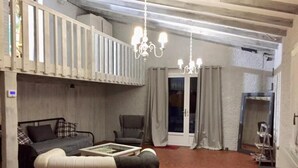 Een woonkamer met een bank, fauteuil en salontafel. Er is een balkon met een hekwerk en een kroonluchter.