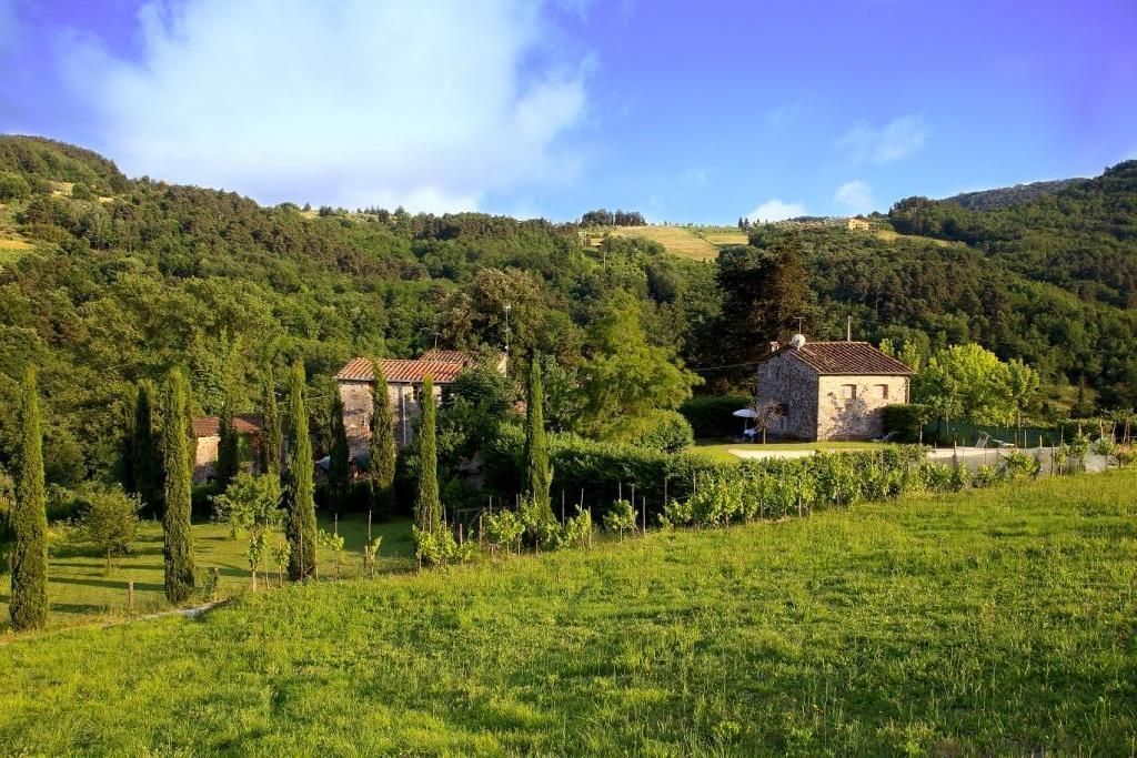 Un paisaje rural con edificaciones de piedra, abundante vegetación y colinas ondulantes.