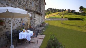 A stone building with a patio table and chairs, surrounded by a well-maintained lawn and a view of rolling hills. - Rustic renovated, with every modern comfort, private pool and garden (Domazzano)