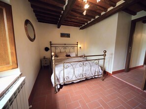Une chambre à coucher avec un lit en métal, une table de chevet, une lampe fixée au mur et une fenêtre avec un cadre en bois.