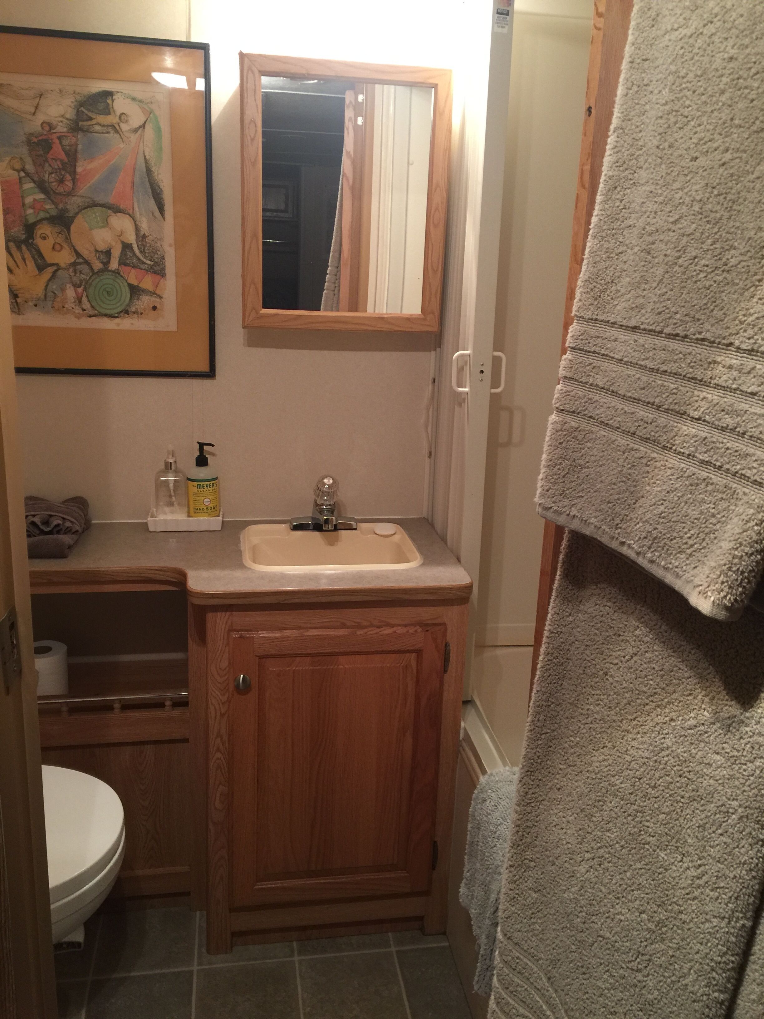A bathroom with a wooden vanity, a sink, a mirror, a toilet, and a towel hanging on the wall.