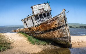 Um naufrágio abandonado numa praia arenosa com água.