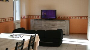 A dining area with a table, chairs, a black sofa, and a television on a cabinet. - accommodation for up to 12 people (Ferrières-Saint-Mary)