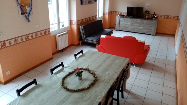 A dining area with a table set for four, a red sofa, a television on a cabinet, and a decorative garland on the table. - accommodation for up to 12 people (Ferrières-Saint-Mary)