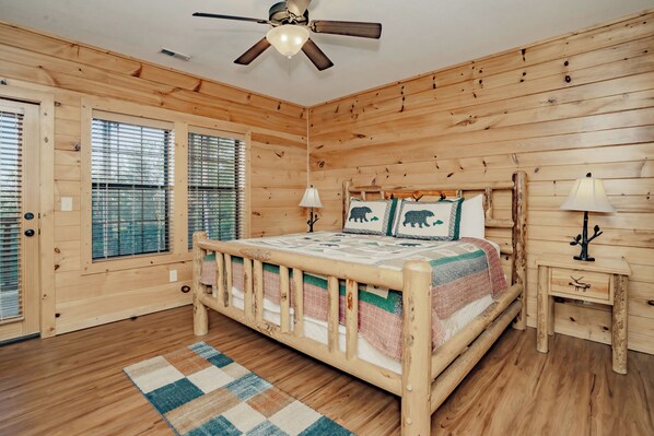 A wooden cabin bedroom with a bed, two bedside lamps, a ceiling fan, and a window with blinds. - A View To Remember: MTN VIEWS! Luxury, Hot Tub, Wifi, Fireplace, Games and more (Sevierville)