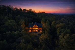 A house surrounded by dense forest with a visible balcony and a chimney.