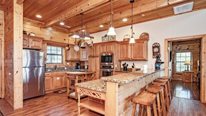 A wooden cabin-style kitchen with a central island, bar stools, wooden cabinets, and a stainless steel refrigerator. - A View To Remember: MTN VIEWS! Luxury, Hot Tub, Wifi, Fireplace, Games and more (Sevierville)