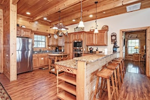 Cocina estilo cabaña de madera con una isla central, taburetes de bar, armarios de madera y un refrigerador de acero inoxidable.