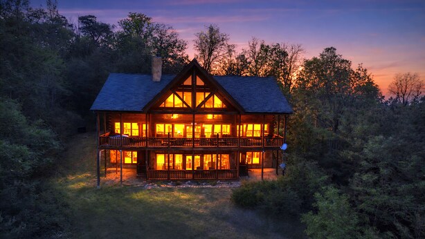 A large, two-story log cabin with multiple windows and a balcony, surrounded by dense forest. - A View To Remember: MTN VIEWS! Luxury, Hot Tub, Wifi, Fireplace, Games and more (Sevierville)