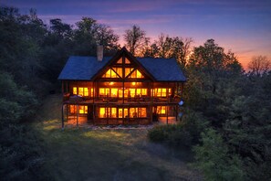 A large, two-story log cabin with multiple windows and a balcony, surrounded by dense forest. - A View To Remember: MTN VIEWS! Luxury, Hot Tub, Wifi, Fireplace, Games and more (Sevierville)