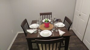 Une table à manger dressée pour quatre personnes, avec des chaises, un set de table en fibres tressées et une petite plante en pot.