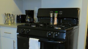 Une cuisine avec un poêle noir, des armoires blanches et une machine à café en acier inoxydable.