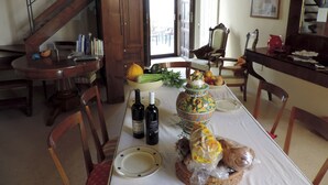 A dining area with a table set for two, featuring a fruit bowl, bread, and bottles.