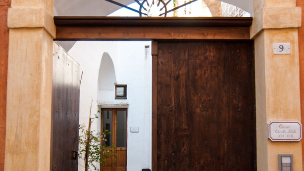 An arched doorway leading to a building with a wooden door and a small window.