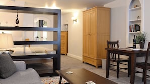 Een gezellige woonkamer met een bank, een bijzettafeltje, een houten kast en een eethoek met stoelen en een tafel.