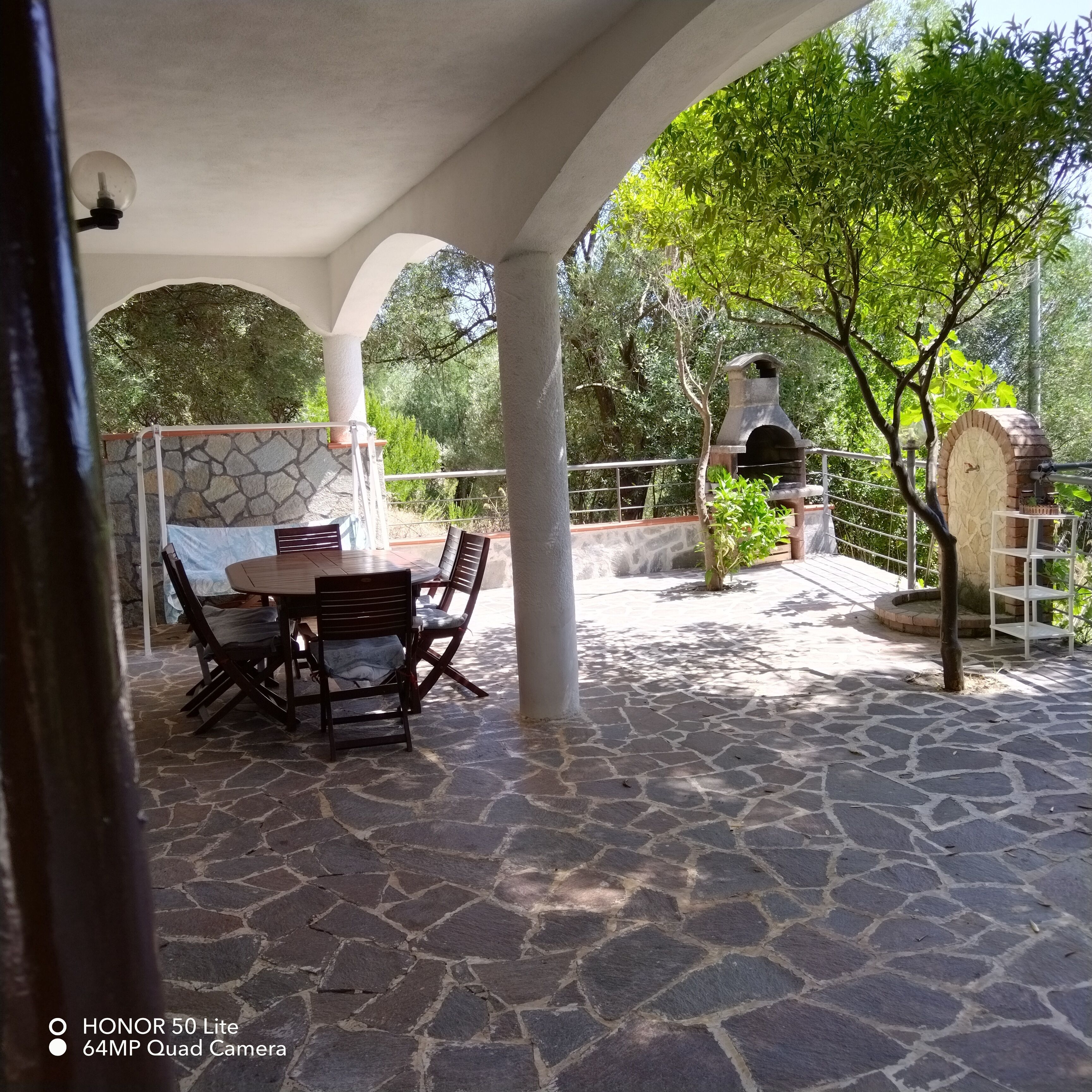 A covered patio with stone flooring, a table with chairs, and a brick oven.