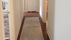 A hallway with a wooden floor and a patterned rug, leading to a white door. - Charming Summer + Fall Football Rental - Near Square & Ole Miss Camp (Oxford)