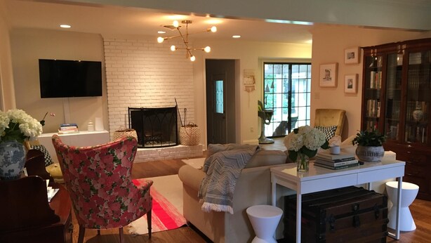 A living room with a fireplace, a television mounted on the wall, a sofa, a coffee table, and a side table with a vase of flowers. - Charming Summer + Fall Football Rental - Near Square & Ole Miss Camp (Oxford)