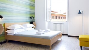 Une chambre moderne avec un lit, une fenêtre donnant sur des immeubles, un radiateur, une lampe et une chaise jaune.