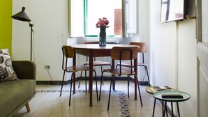 Un coin repas avec une table ronde, quatre chaises, un vase avec des fleurs, une lampe, un canapé et une petite table avec une télécommande.