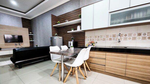 A modern kitchen with a dining area, featuring a marble countertop, white chairs, and wooden cabinets. - Ouma Guest House (Bandung)