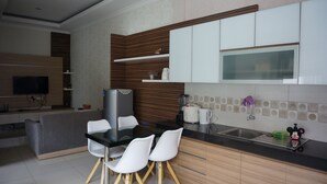 A modern kitchen with a dining area, featuring a flat-screen TV, a refrigerator, a coffee maker, and a sink. - Ouma Guest House (Bandung)