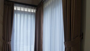A hotel room with a bed, a bench at the window, and curtains. - Ouma Guest House (Bandung)