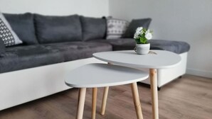Un salon moderne avec un canapé gris, une table basse blanche aux pieds en bois et une petite plante en pot posée sur la table.