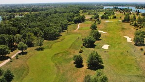 Vue aérienne d’un parcours de golf avec des bunkers de sable, des arbres et un lac en arrière-plan.