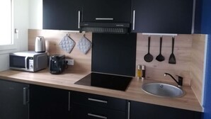 Une cuisine moderne avec des meubles de couleur noire, une cuisinière encastrée, un four à micro-ondes, une bouilloire et un évier.