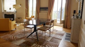A spacious living room with a round glass table, comfortable seating, a fireplace, and large windows with curtains. - ST GERMAIN, BALCONY, VIEW, 2 BATHS, 30–60 days ahead? Private offer. BEV-VBs (Paris)