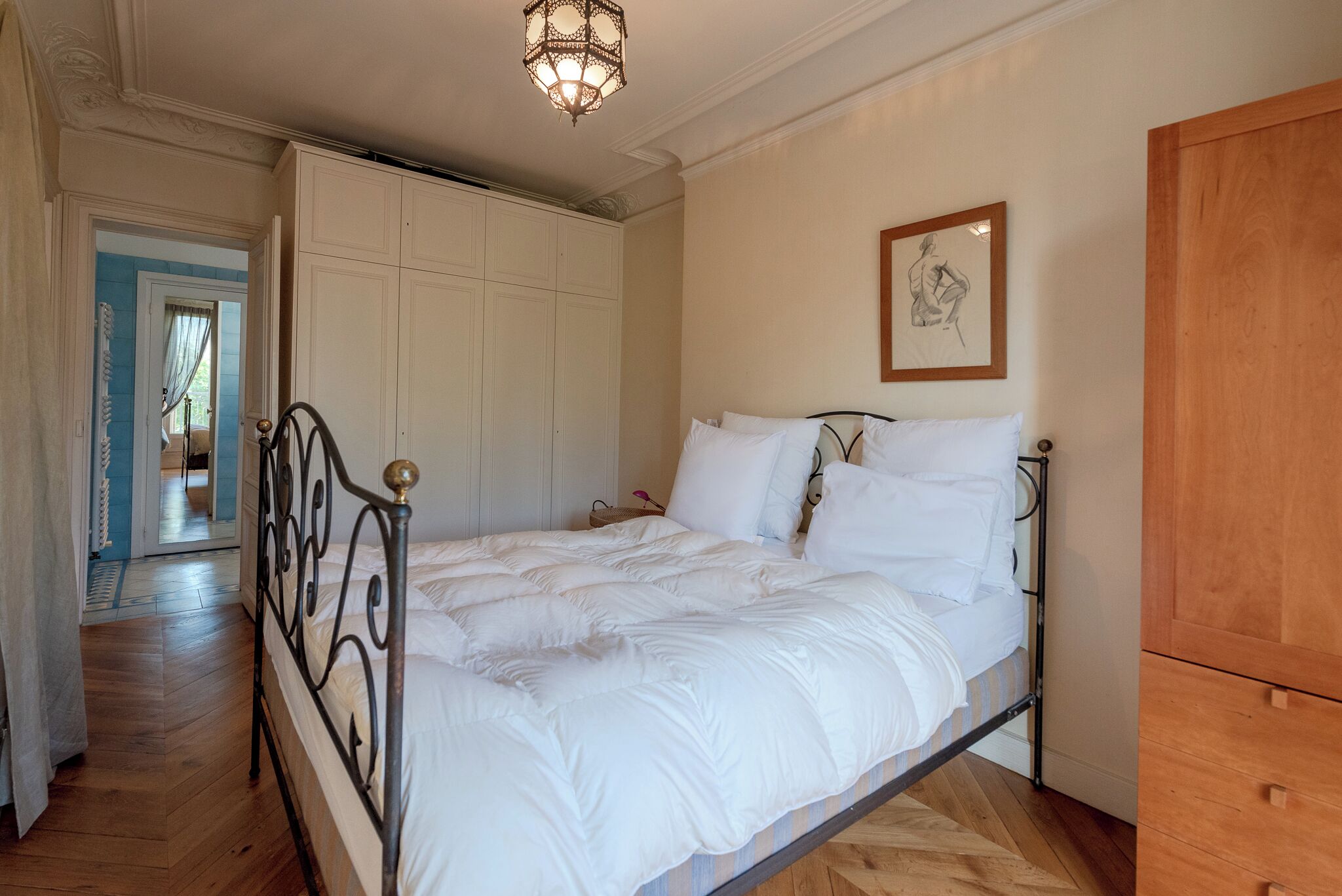 Un dormitorio con cama, armario de madera, cuadro enmarco y puerta que da a otra habitación.