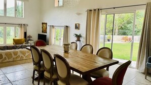 Un comedor con una mesa y sillas de madera, una araña y ventanas grandes con cortinas.