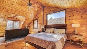 Een houten slaapkamer met een groot bed, een bankje en uitzicht op het bos door een raam.