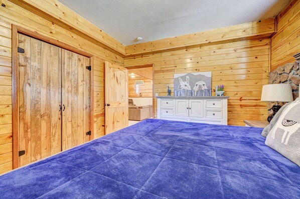 A room with wooden walls, a bed with a blue bedspread, a white dresser, and a painting of llamas on the wall. - 2 Mountain Cabins on 40 acres (florissant)