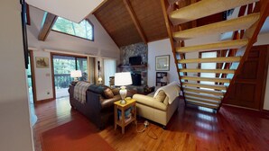 A spacious living area with a stone fireplace, wooden flooring, and a wooden staircase.
