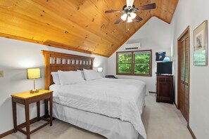 Un dormitorio con techo de madera, una cama, una mesita de noche, una lámpara, un televisor y una ventana con vistas a zonas verdes.