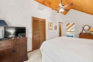 Un dormitorio con cama, televisor, armario de madera, ventilador de techo y puerta que da a un área exterior.