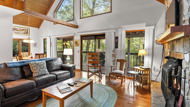 A spacious living room with a fireplace, leather sofa, wooden coffee table, and large windows.