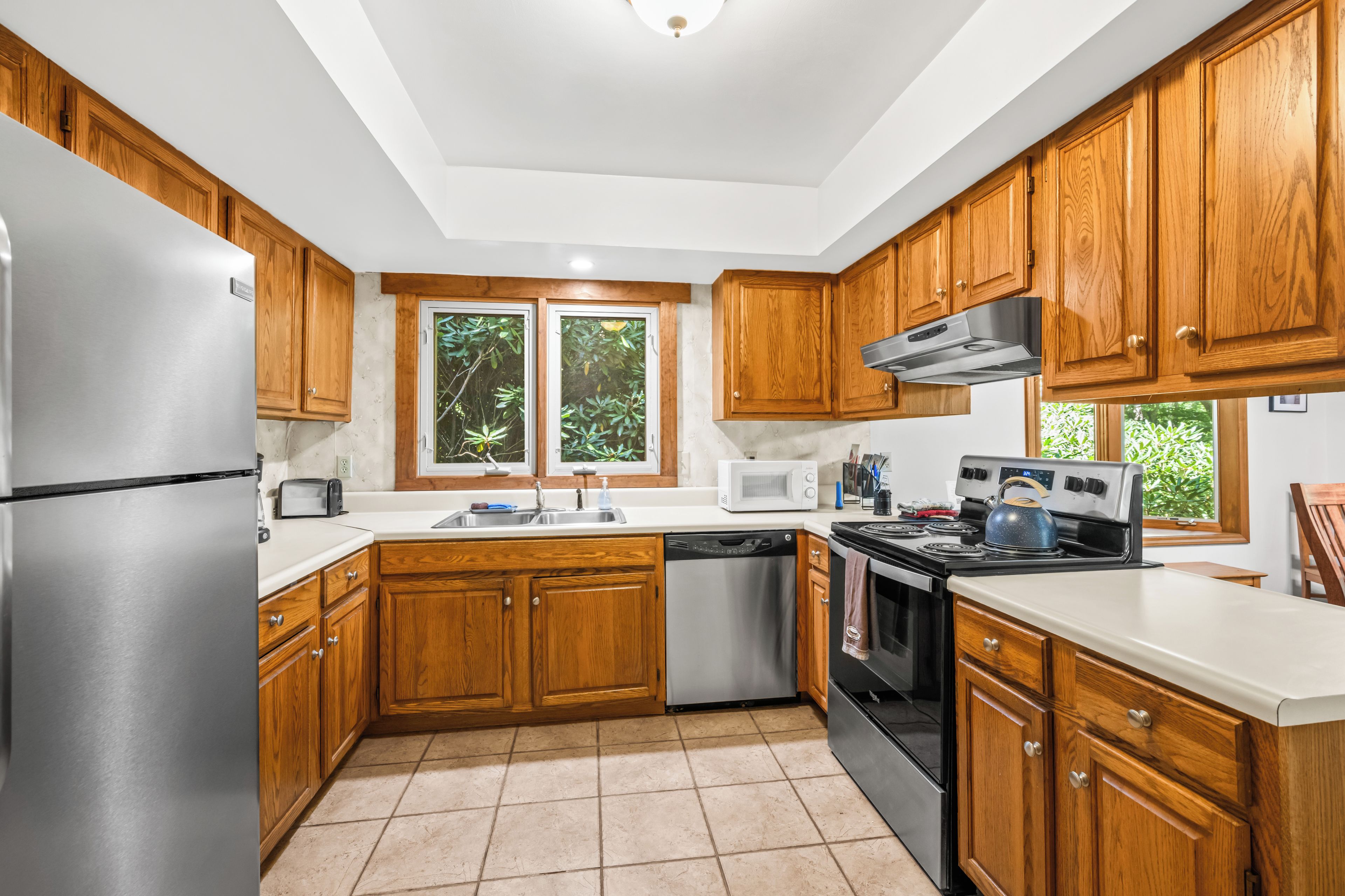 A kitchen with wooden cabinets, stainless steel appliances, a dishwasher, and a window with a view of greenery.