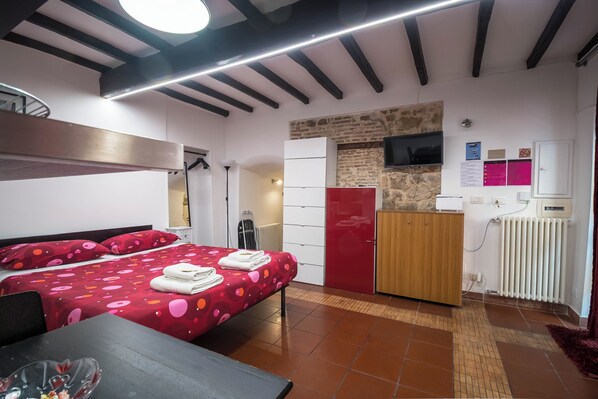 Habitación de hotel con cama, escritorio, armario, radiador y televisor en la pared.