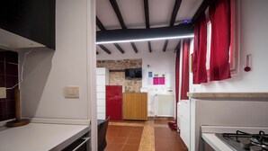 A narrow kitchen with a tiled floor, a gas stove, a wooden cabinet, and a red curtain. - independent apartment in Trastevere (Roma)