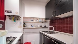 A compact kitchen with a gas stove, a sink, and a red trash bin. - independent apartment in Trastevere (Roma)