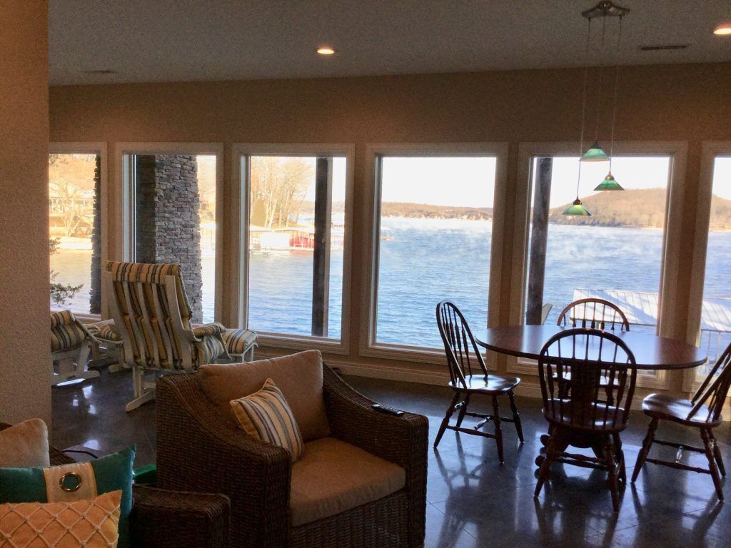 A room with large windows overlooking a body of water, wicker furniture, and a stone pillar.