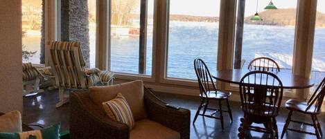A room with large windows overlooking a body of water, wicker furniture, and a stone pillar.